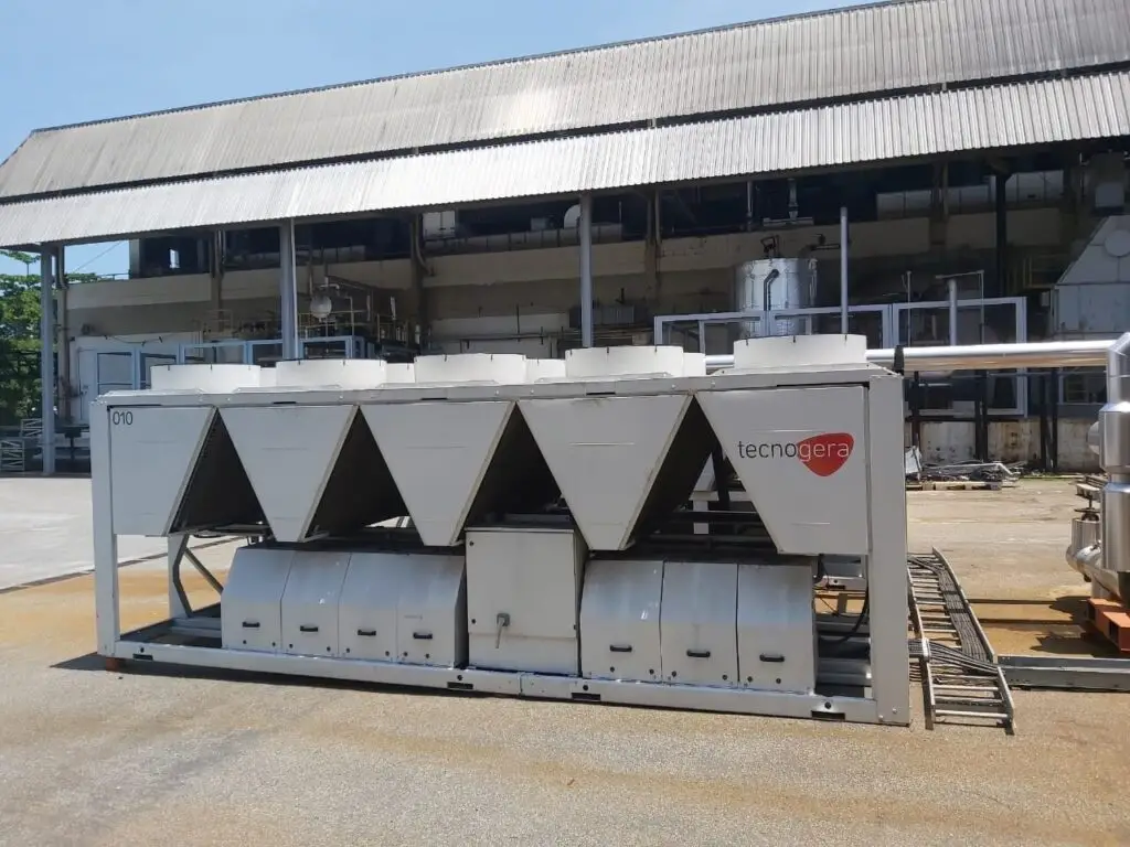 Chiller industrial Tecnogera ao ar livre, com ventiladores e dutos cônicos, em frente a prédio antigo; ideal para manutenção.