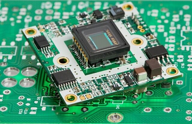 Centralizado em uma placa verde, o sensor de imagem com vidro é rodeado por microchips e conectores.