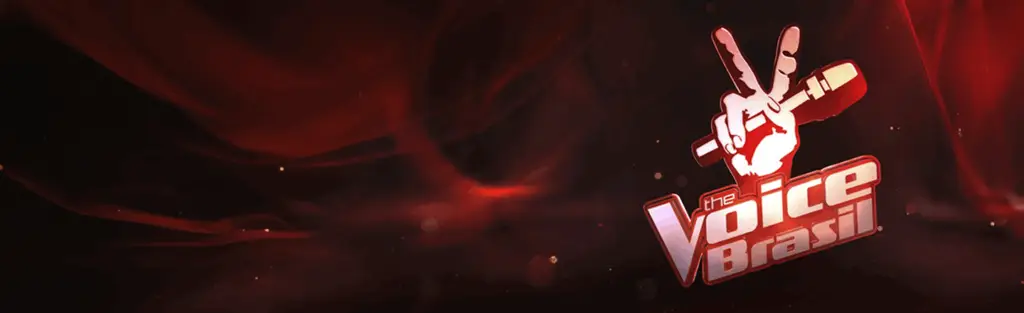 Imagem do logotipo do "The Voice Brasil" sobre um fundo vermelho escuro com efeito esfumaçado. A mão clássica fazendo o sinal de paz segura um microfone, e ao lado direito está o nome "The Voice Brasil" em destaque, com letras brancas e vermelhas. Esse visual é utilizado no portal da Tecnogera.