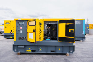 Um gerador amarelo está posicionado ao ar livre sobre uma superfície de concreto. As portas frontais estão abertas, revelando os componentes internos do equipamento. Esses geradores garantem segurança 24 horas por dia, sendo ideais para o setor hospitalar