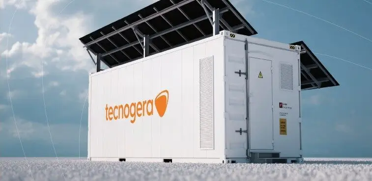 Um contêiner branco com o nome Tecnogera em letras laranja, equipado com painéis solares no telhado, está posicionado sobre uma superfície coberta de neve sob um céu parcialmente nublado. A cena destaca seu uso como solução portátil de geração de energia renovável.