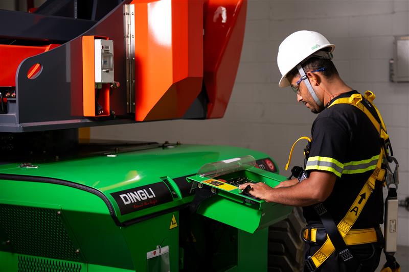 Profissional da Tecnogera, com capacete e cinto, opera plataforma em ambiente industrial, realizando manutenção.