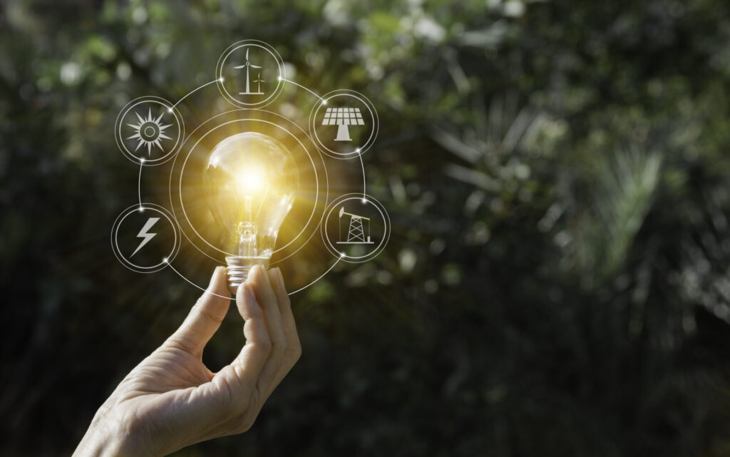 Uma mão segura uma lâmpada acesa, com ícones de energia limpa ao redor, representando a transição energética.