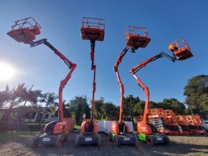 Equipamentos Tecnogera: quatro plataformas articuladas vermelhas elevadas sob céu azul, com palmeiras e equipamentos ao redor.