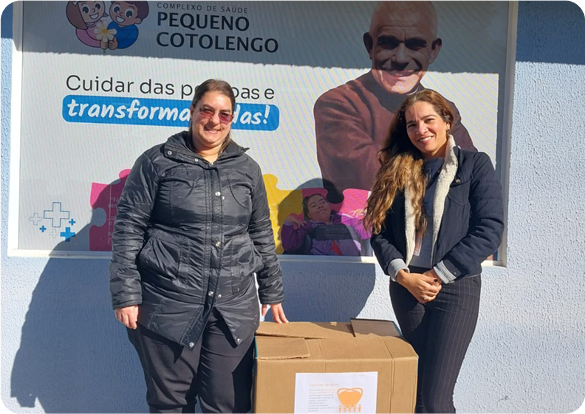 Duas mulheres sorrindo em frente à placa Pequeno Cotolengo, ação social com apoio da Tecnogera. No destaque: "Cuidar das pessoas e transformar vidas!".