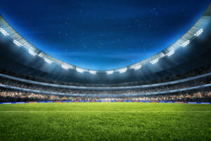 O estádio moderno iluminado da Copa do Mundo, com gramado verde e arquibancadas vazias sob o céu estrelado.
